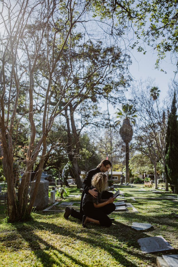 story-02 Two women embracing in a sunlit cemetery surrounded by trees.